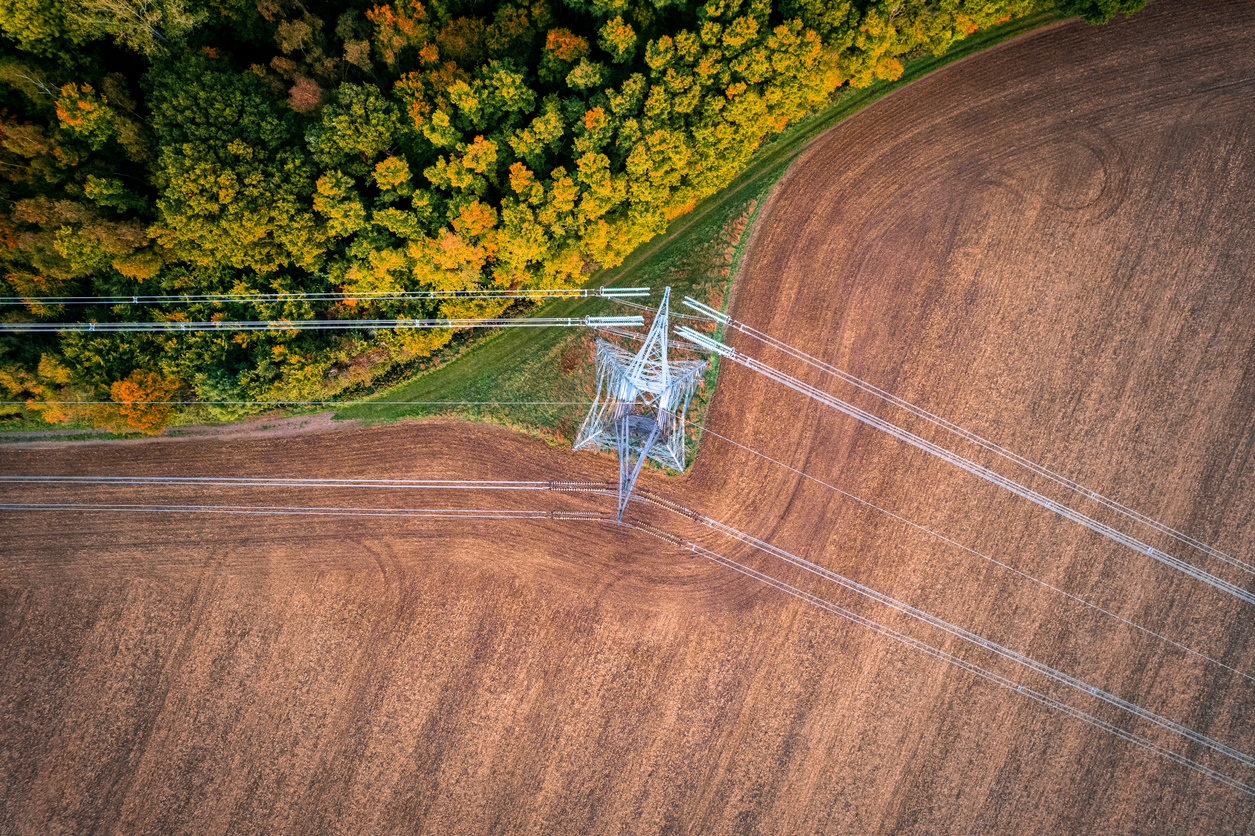 400kV extra high voltage electricity line changing direction above cultivated field contracting with autumn forest, shot from above.